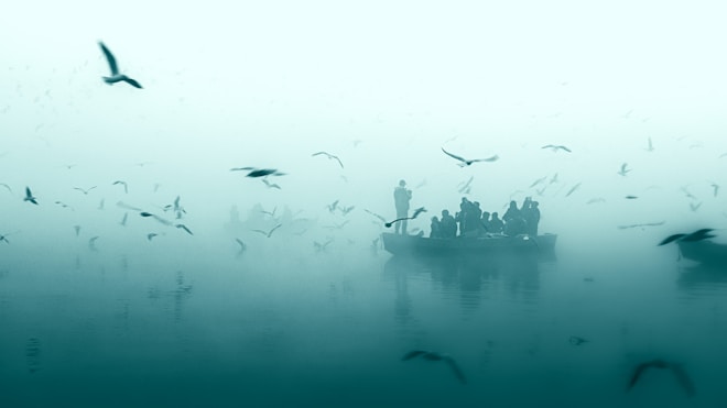 A serene and misty scene with a group of people on a boat surrounded by many birds flying in the foggy air. The calm water reflects the silhouettes of the boat and birds, creating a tranquil and ethereal atmosphere.