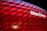 The image features the Allianz Arena with its illuminated exterior panels creating a vibrant red glow. The stadium's name is prominently displayed in white on a section of the facade.