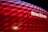 The image features the Allianz Arena with its illuminated exterior panels creating a vibrant red glow. The stadium's name is prominently displayed in white on a section of the facade.
