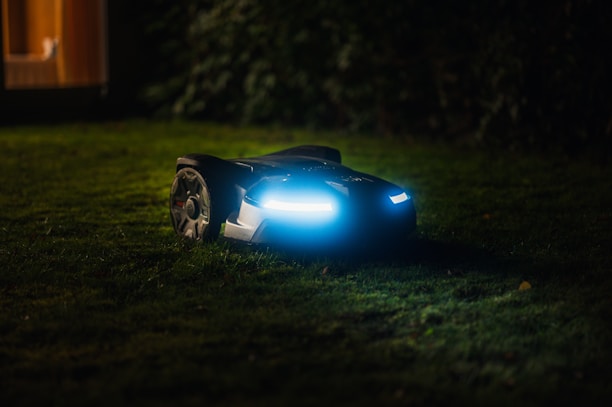 Close-up of a robotic mower navigating a right-of-way with green grass and safety cones nearby.
