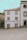 A quaint building with white walls and brown trim features the words 'Casa do Bom Café' in large letters on the front. It is situated in a quiet, partially paved square and is flanked by other traditional stone buildings.