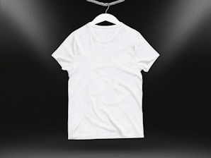 A plain white t-shirt on a hanger against a dark background. Soft lighting highlights the texture and folds of the fabric.