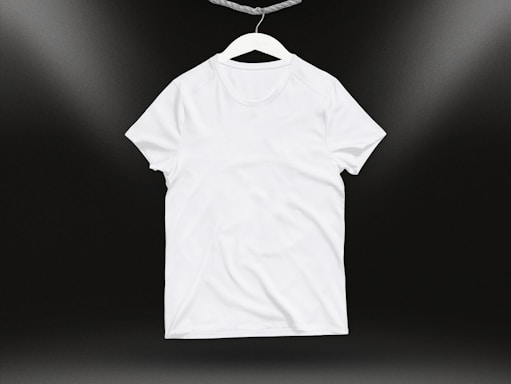 A plain white t-shirt on a hanger against a dark background. Soft lighting highlights the texture and folds of the fabric.
