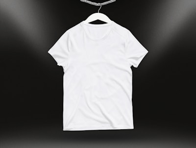 A plain white t-shirt on a hanger against a dark background. Soft lighting highlights the texture and folds of the fabric.
