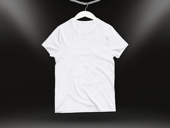 A plain white t-shirt on a hanger against a dark background. Soft lighting highlights the texture and folds of the fabric.
