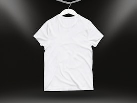 A plain white t-shirt on a hanger against a dark background. Soft lighting highlights the texture and folds of the fabric.