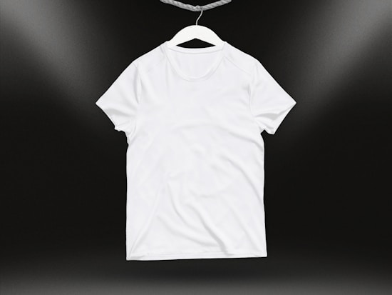 A plain white t-shirt on a hanger against a dark background. Soft lighting highlights the texture and folds of the fabric.