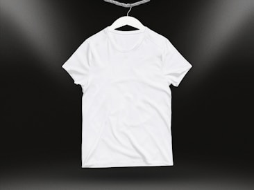 A plain white t-shirt on a hanger against a dark background. Soft lighting highlights the texture and folds of the fabric.