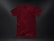 A plain, deep red t-shirt placed against a dark textured background. The garment appears to be crumpled slightly, showing natural folds and shadows. The fabric looks soft, and the shirt is displayed in a casual, relaxed style.