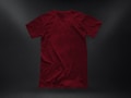 A plain, deep red t-shirt placed against a dark textured background. The garment appears to be crumpled slightly, showing natural folds and shadows. The fabric looks soft, and the shirt is displayed in a casual, relaxed style.