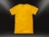 A plain yellow t-shirt is centered against a dark background, illuminated by subtle light gradients in the corners. The shirt is neatly laid out, highlighting its texture and smooth fabric.