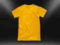 A plain yellow t-shirt is centered against a dark background, illuminated by subtle light gradients in the corners. The shirt is neatly laid out, highlighting its texture and smooth fabric.