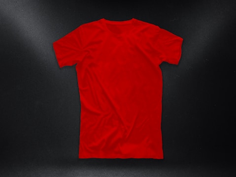 A plain red T-shirt is laid out against a dark background, with subtle lighting highlighting its texture and shape.