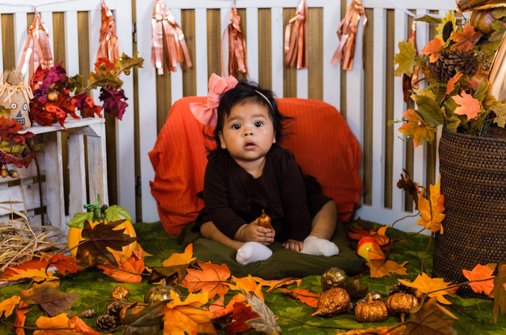 a little girl sitting on a bed surrounded by fall leaves