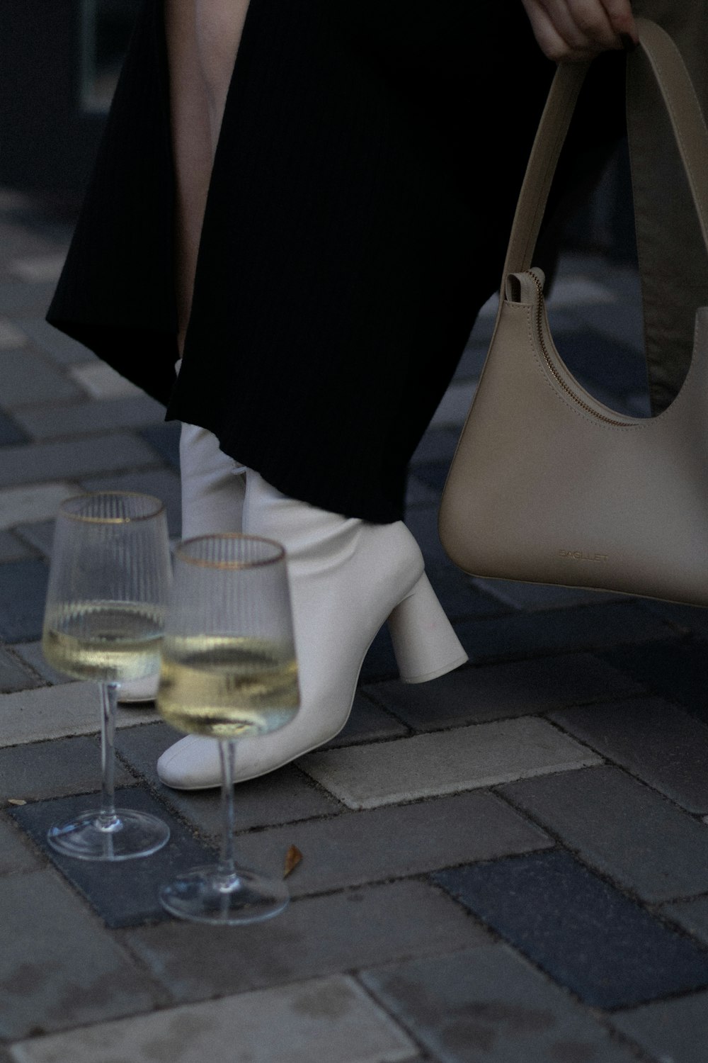a woman is holding a purse and two glasses of wine