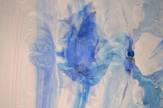 A fluid, abstract painting features swirling patterns of blue and white, with a predominant darker blue shape in the center resembling a petal or leaf. Soft lines and blending create a calming, rhythmical flow across the canvas.