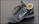 A single black leather sports shoe, featuring a swoosh design on its side. The shoe has black laces loosely tied and a beige inner lining visible at the ankle. It appears slightly worn, with dirt marks on the sole and creases in the leather.