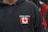 A black hoodie features a patch with the Canadian flag and the words 'Stand United' on the chest. The hoodie includes drawstrings and a red star design on the sleeve.