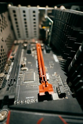 A close-up view of a computer motherboard featuring various components including a red PCIe slot. The circuit board is populated with numerous small electronic parts, and the lighting highlights the details of the technology.