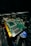 A close-up view of a computer graphics card with visible electronic components and connectors. The circuit board is green with gold connectors and several black chips. Part of a cooling fan with the Intel logo is visible beneath the card, along with visible wiring.