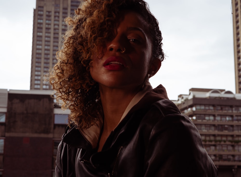 a woman with curly hair standing in front of tall buildings