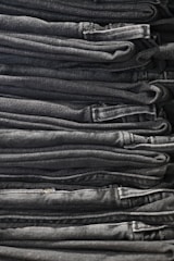 A neatly arranged stack of folded dark gray and black denim jeans, showing clean lines and uniformity.