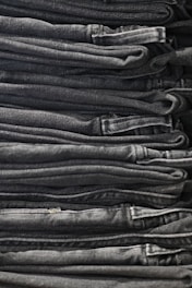 A neatly arranged stack of folded dark gray and black denim jeans, showing clean lines and uniformity.