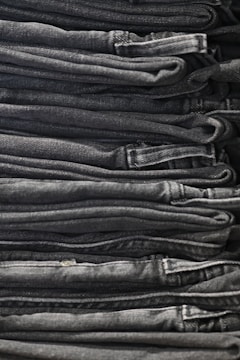 A neatly arranged stack of folded dark gray and black denim jeans, showing clean lines and uniformity.