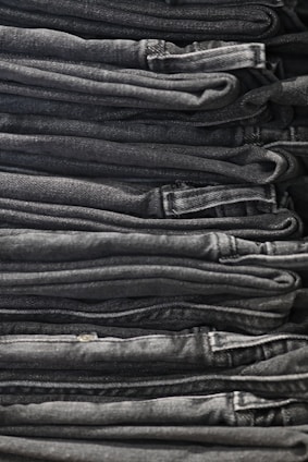 A neatly arranged stack of folded dark gray and black denim jeans, showing clean lines and uniformity.