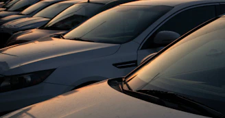 A row of fuel-efficient economy cars parked neatly outside a service garage at sunset.