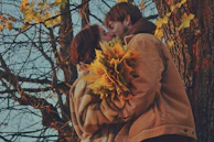 A family sharing a quiet embrace under terracotta-colored autumn leaves.