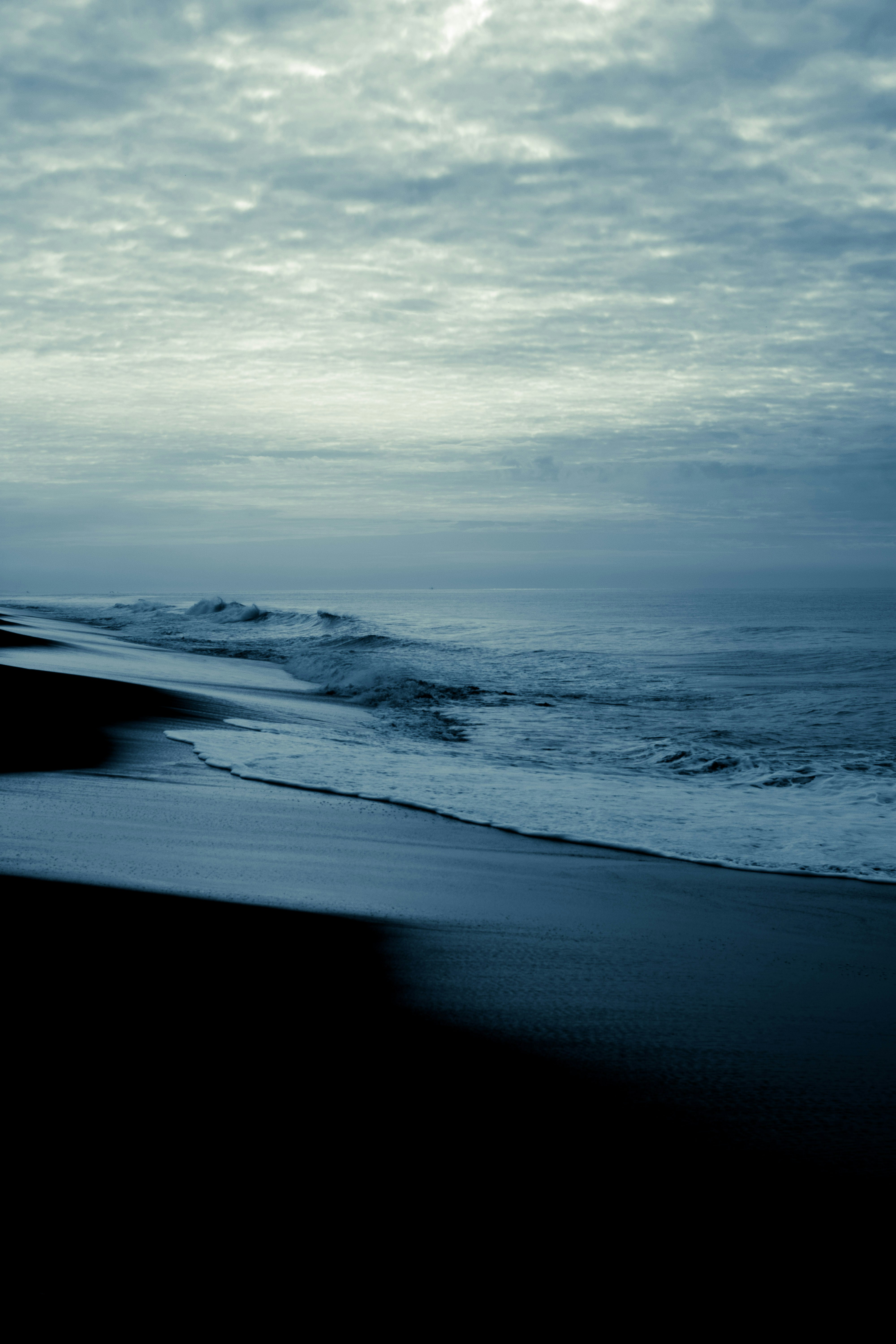 Dutch Zeeland coastline with wide flat beach and dramatic cloudy sky, dark stormy atmosphere, deep shadows on shallow lagoon water, moody low-key lighting