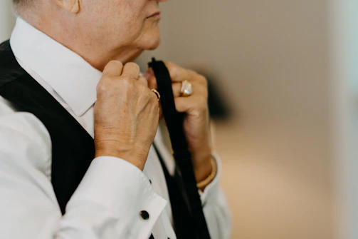 Close-up of a groom adjusting his tie, with soft natural light highlighting the details.