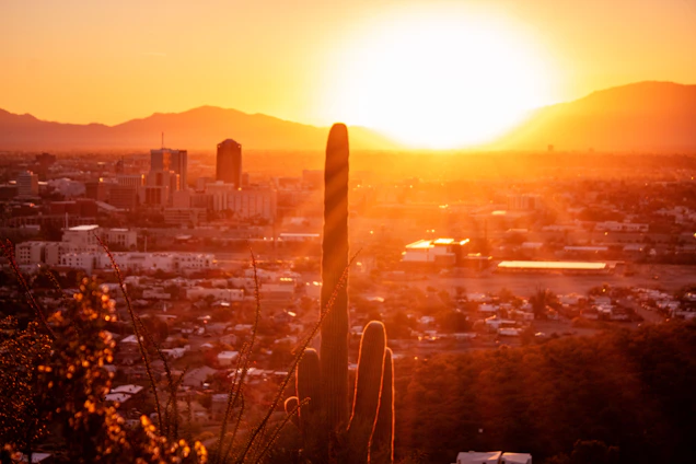A warm sunset over Tucson with a modern home silhouette in the foreground.