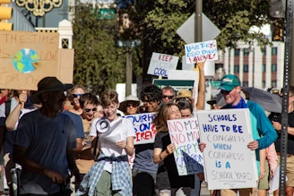 A group of people participating in a protest march, holding various signs with messages related to environmental issues. A person in the foreground is holding a megaphone, while others are smiling and actively engaging in the demonstration.