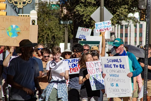A group of people participating in a protest march, holding various signs with messages related to environmental issues. A person in the foreground is holding a megaphone, while others are smiling and actively engaging in the demonstration.