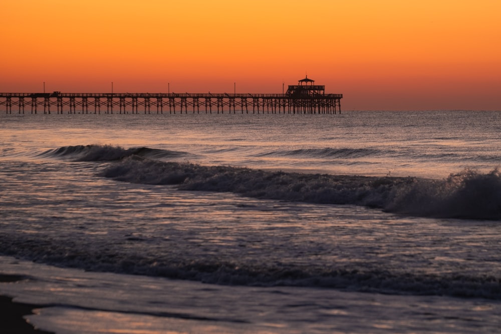 a pier at sunset with waves crashing in front of it