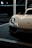 A sleek and modern sports car with a shiny white exterior and prominent headlights. The car is partially visible, positioned in a well-lit indoor setting, possibly on display or at an event. The logo is visible on the front, and a license plate with event details is mounted below.