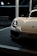 A sleek and modern sports car with a shiny white exterior and prominent headlights. The car is partially visible, positioned in a well-lit indoor setting, possibly on display or at an event. The logo is visible on the front, and a license plate with event details is mounted below.