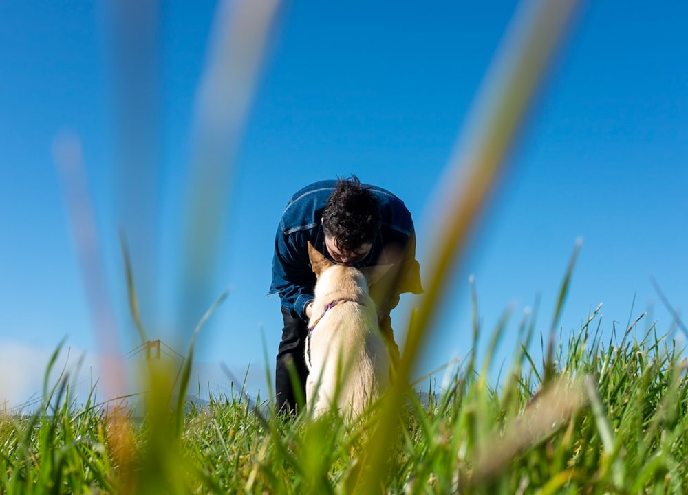a man kneeling down next to a dog on a lush green field