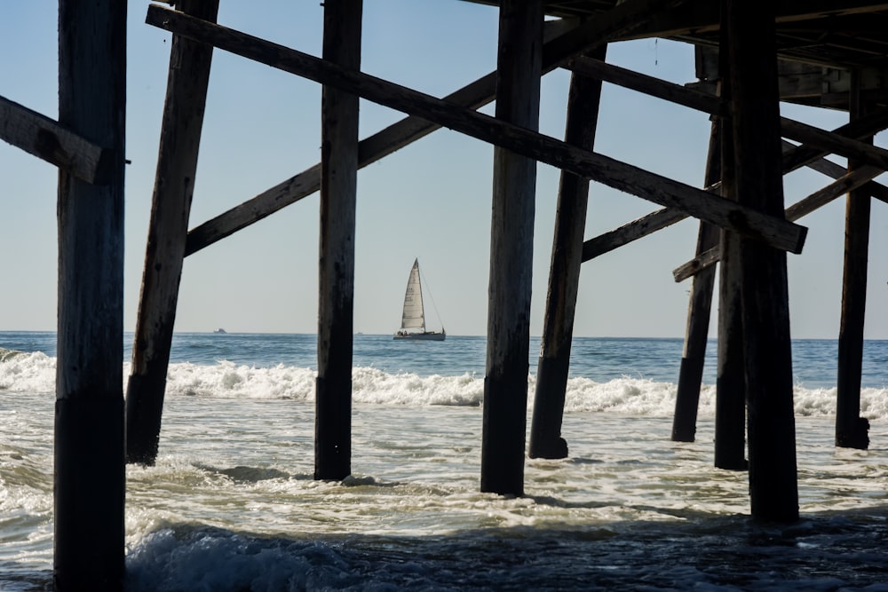 a sailboat in the ocean under a pier