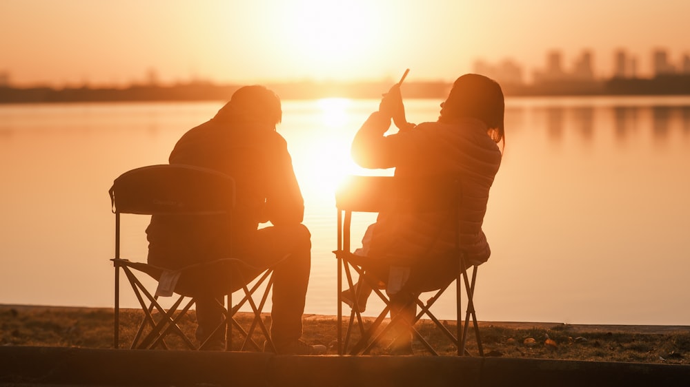 a couple of people sitting in chairs near a body of water