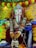 A beautifully adorned statue of the Hindu deity Ganesha is surrounded by vibrant marigold and chrysanthemum flowers. The statue is intricately detailed with an ornate crown and jewels, holding various objects, and there is a colorful textile backdrop adorned with decorative floral patterns.