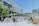 A lively outdoor area with groups of people walking and interacting near a modern building with a large screen displaying nature-themed images. Several market stalls or stands line the area, and lush greenery decorates parts of the building facade, adding a natural touch to the urban setting.
