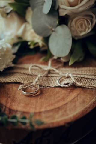 Close-up of wedding rings resting on a rustic wooden table surrounded by soft greenery.