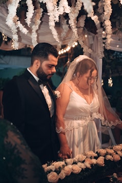 Couple exchanging vows under a floral arch with friends and family watching.
