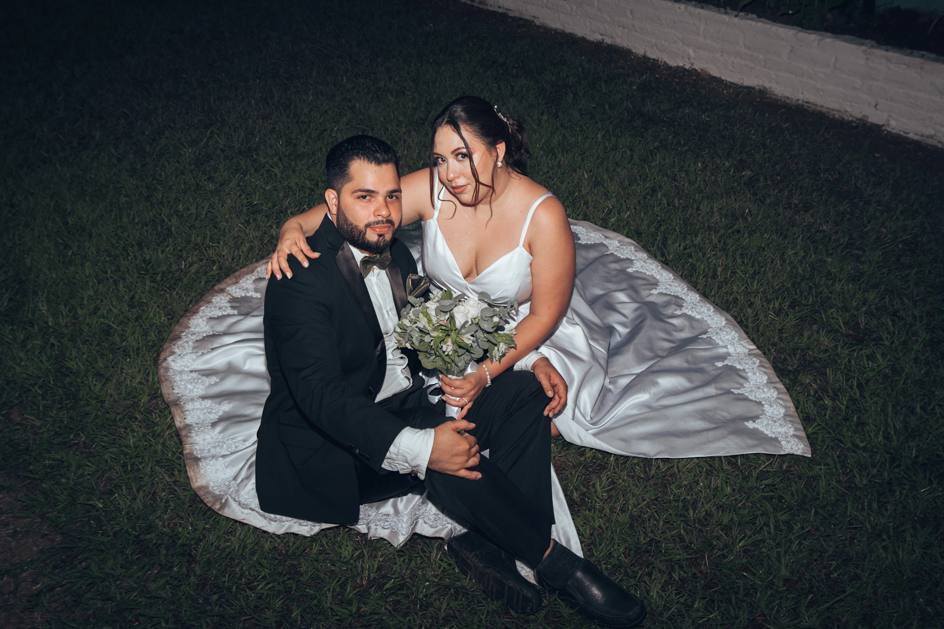 a bride and groom sitting on a blanket in the grass