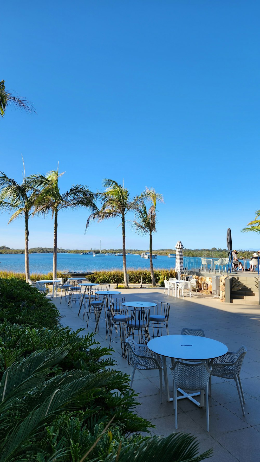 a patio with tables and chairs next to a body of water