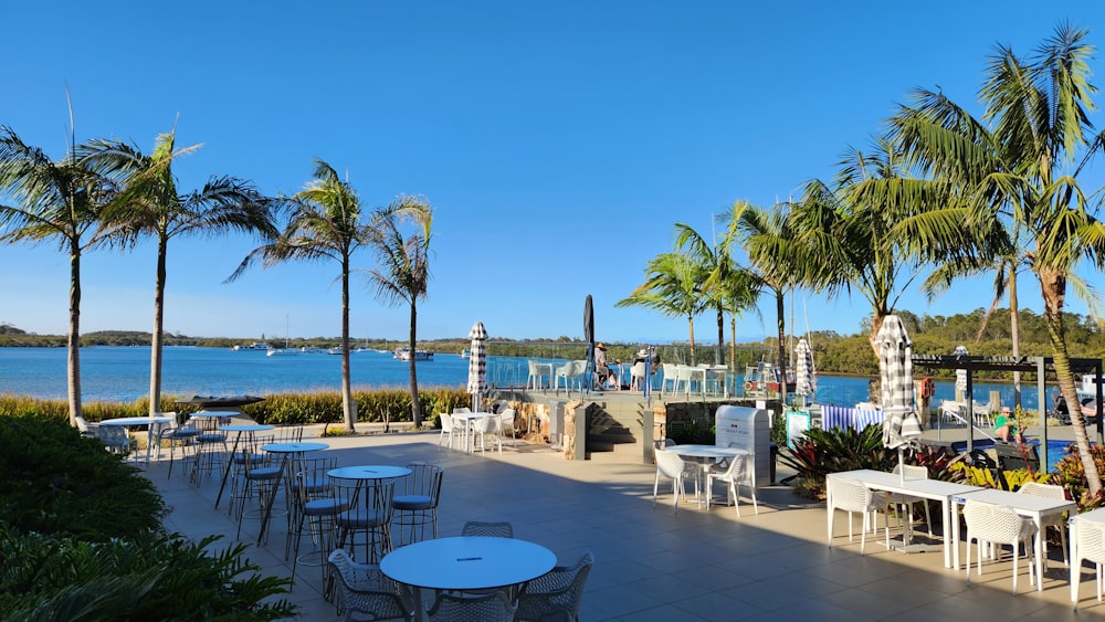 a patio with tables and chairs next to a body of water