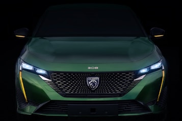 A sleek, modern car with a glossy green exterior, featuring sharp, angular LED headlights and a prominent front grille with the Peugeot logo. The design is aerodynamic and aggressive, emphasizing performance.
